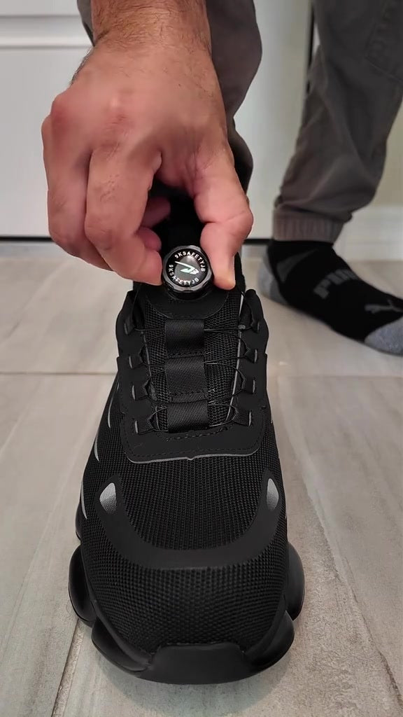 Fingers pinching the SteelTurn dial-lock knob on the tongue of the safety sneaker
